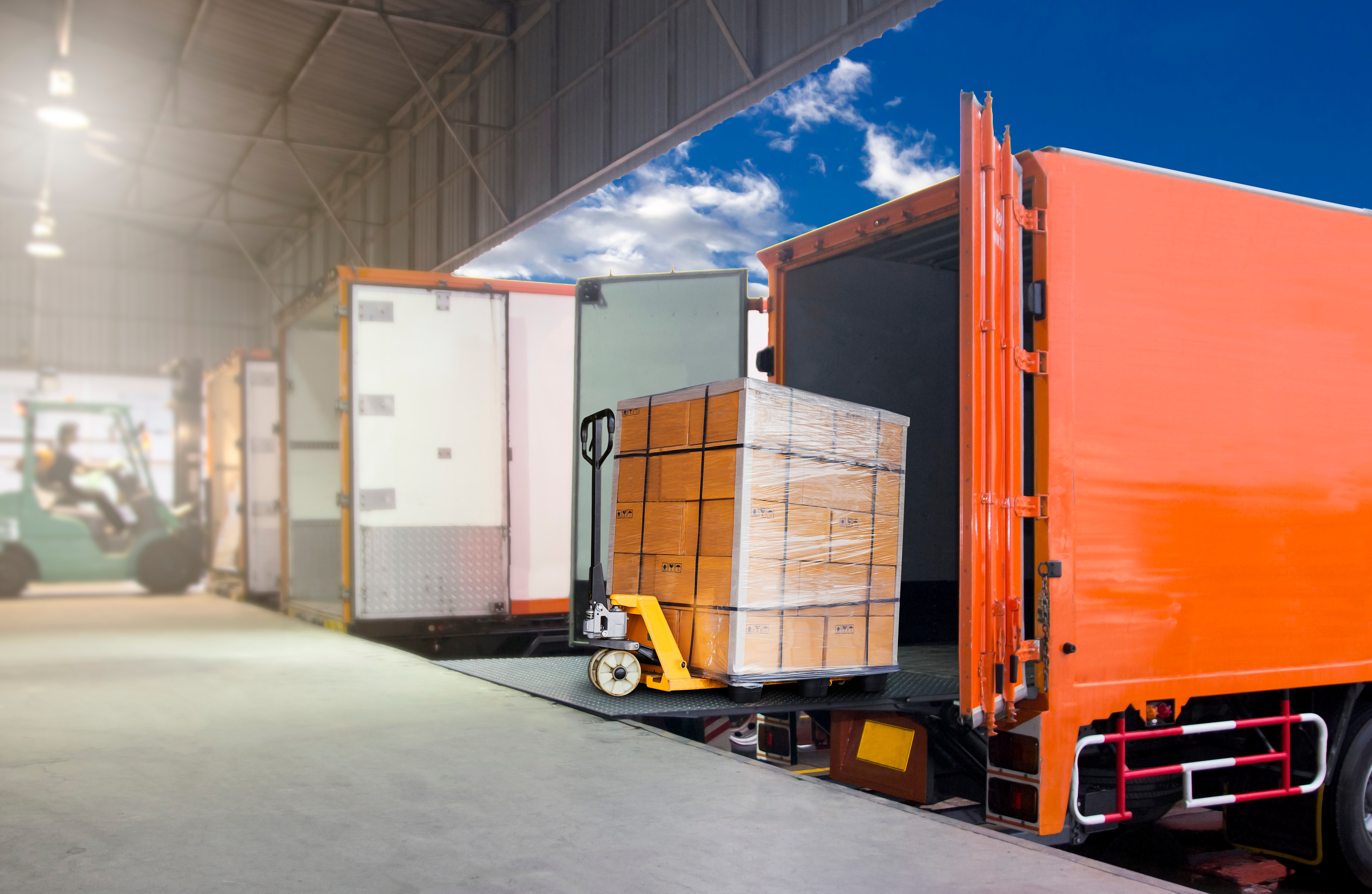 Loading dock scene with a pallet jack moving boxes into an orange truck. Forklift in background, blue sky visible through open door.