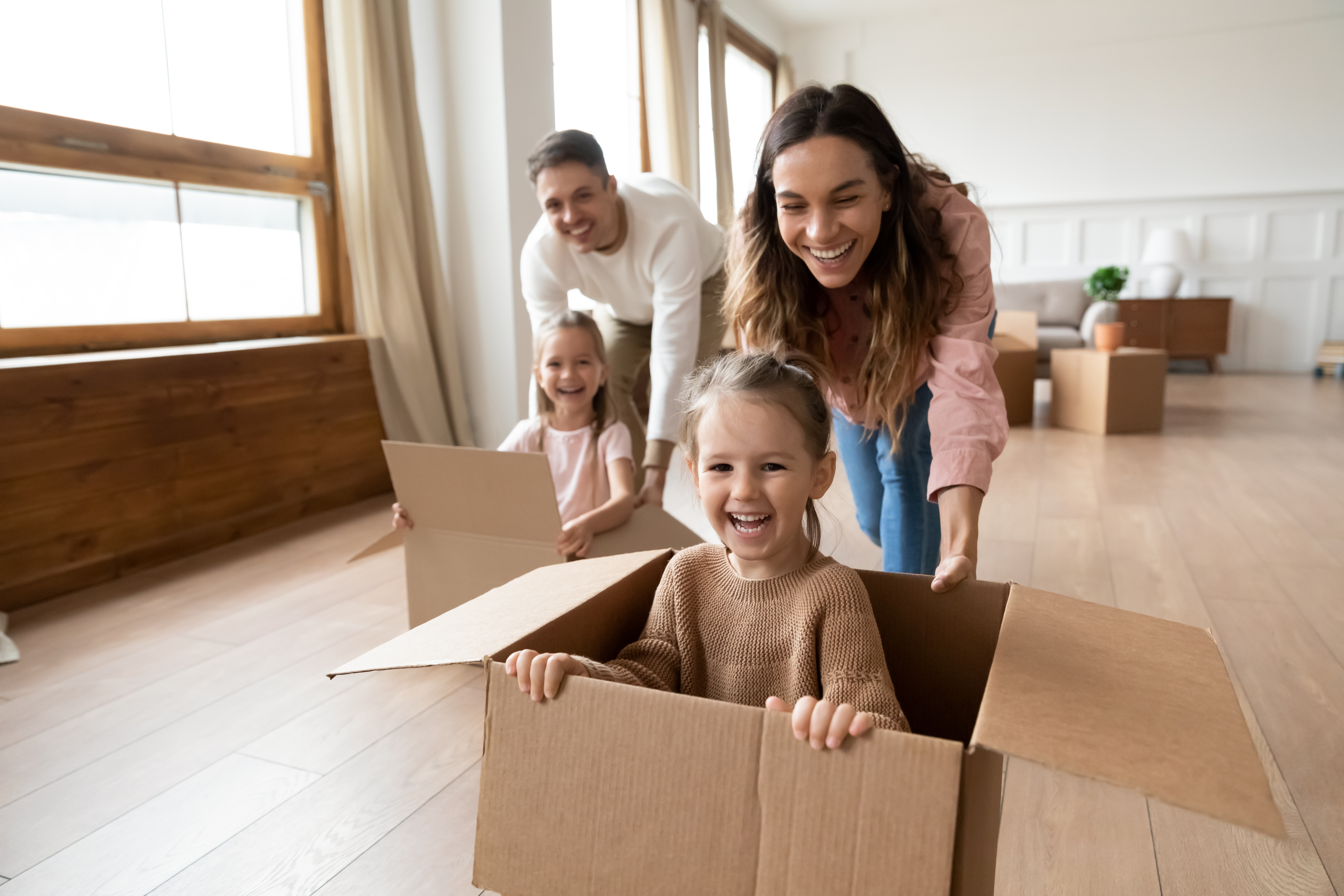 Happy parents playing with cute small kids daughters laughing on moving day, family tenant