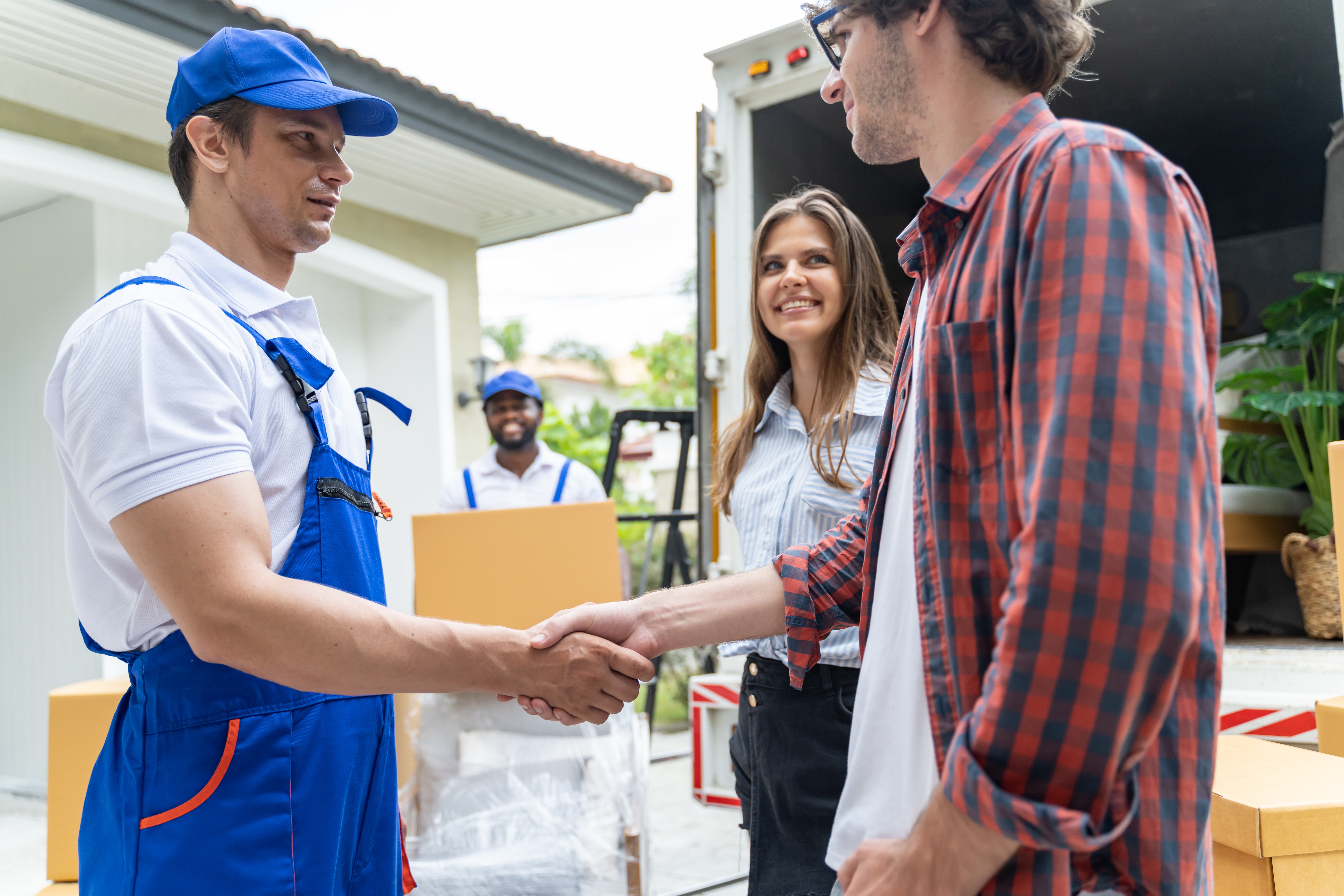 Affordable mover shaking customers hand while another mover is unloading boxes.