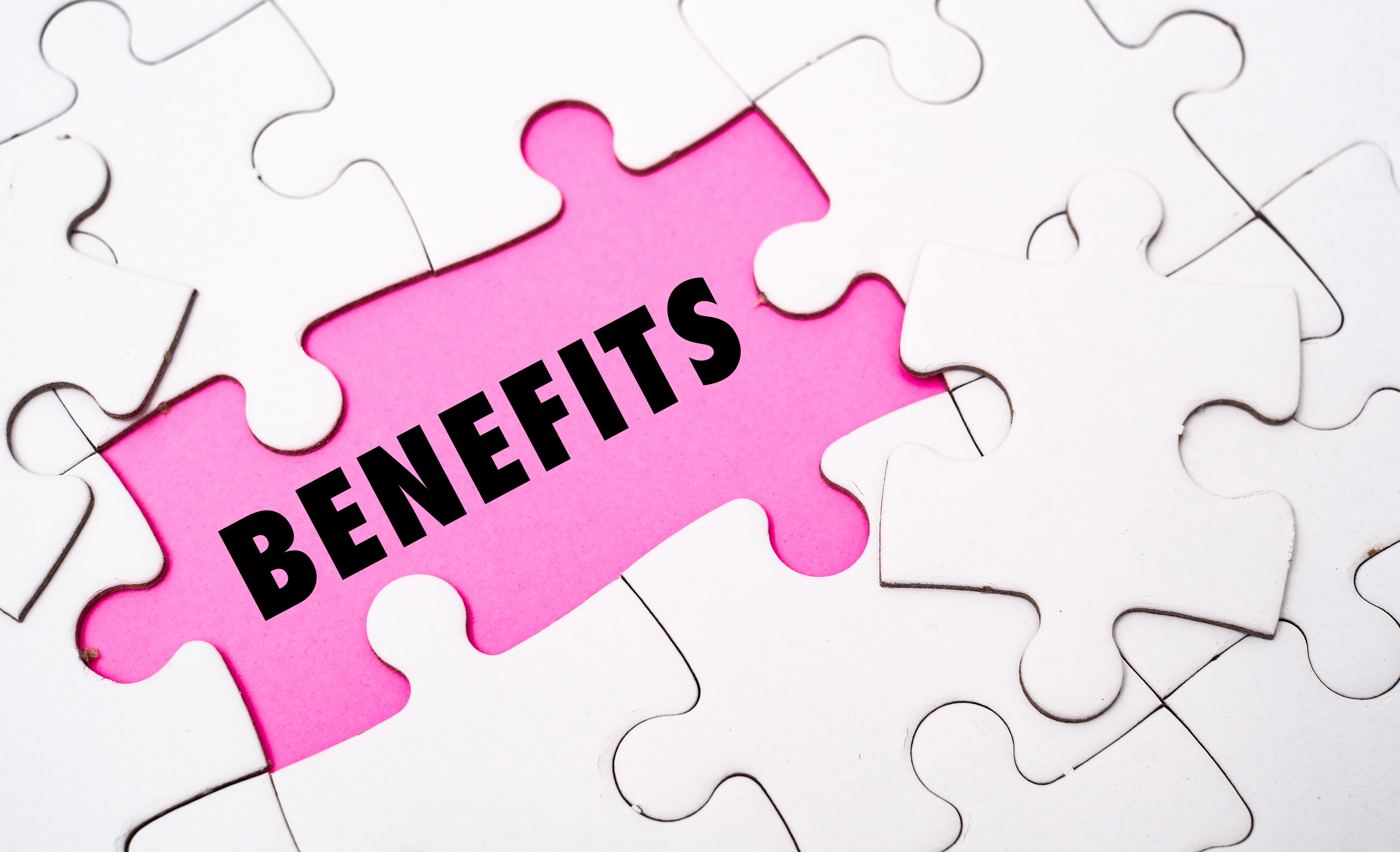 White puzzle pieces on pink background, with the word "BENEFITS" in bold black text. Piece missing, creating focus on the word.