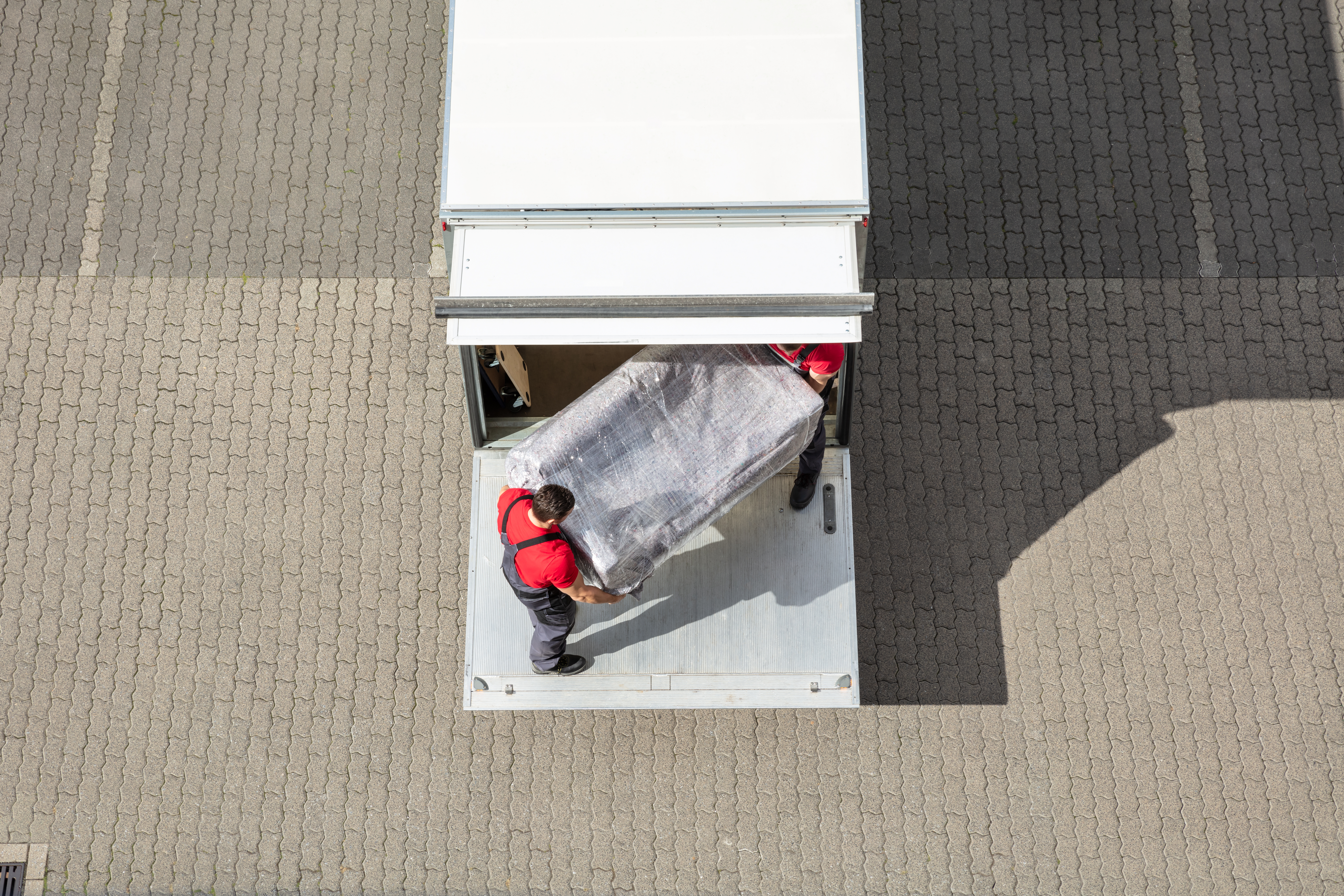 An Elevated View Of Male Mover Unloading The Furniture From Truck On Cobblestone Pavement.